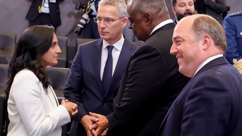 A woman in a white jacket speaks to three men in suits.