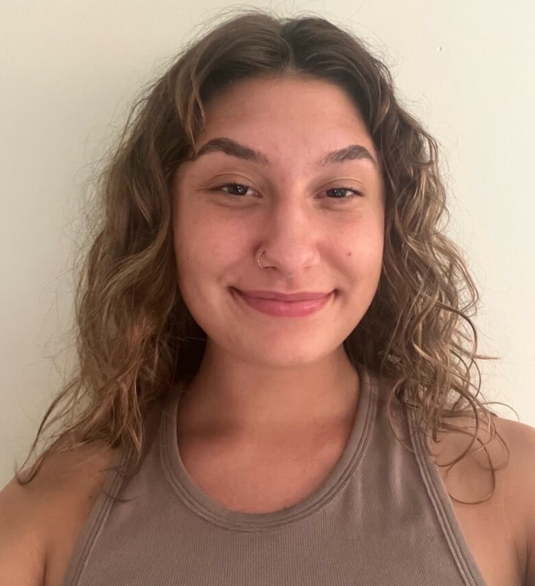 A woman with light brown curly hair and A brown tank top.