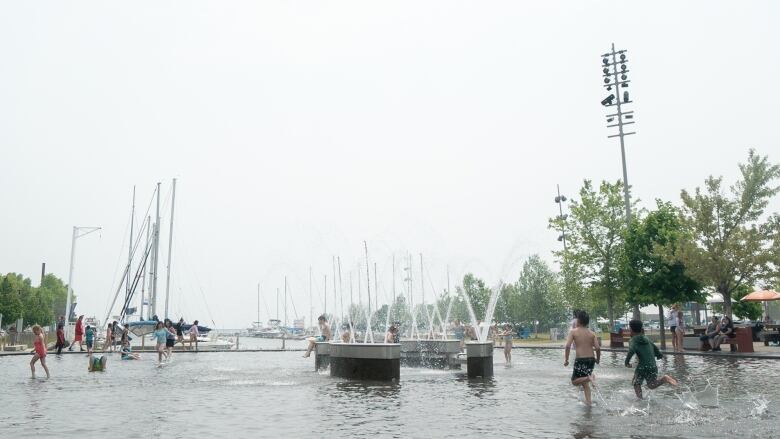 Kids are running around in the Marina Park splash pad during a smoke-filled day.