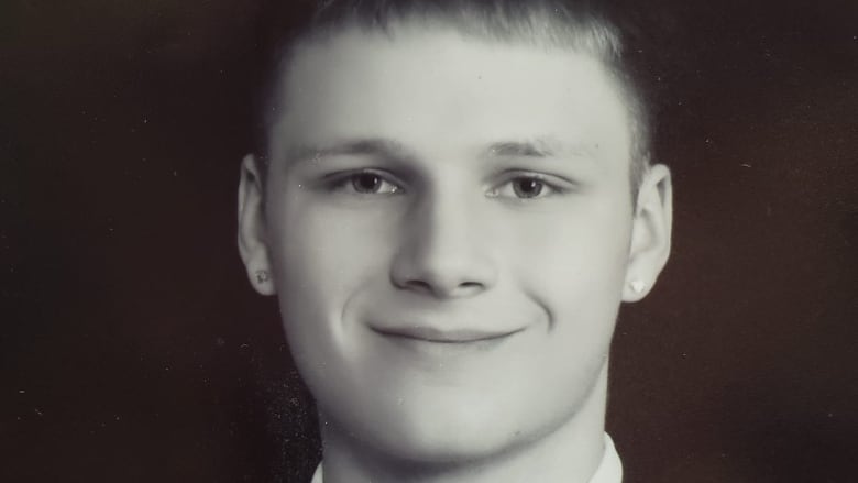 A clean-cut looking teenager smiles at the camera with a suit on.