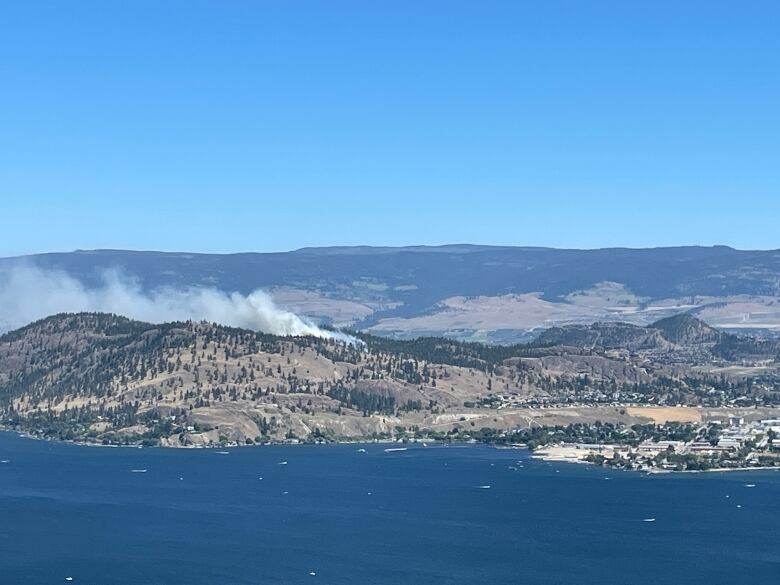 Smoke rises from a hilltop next to a lake.