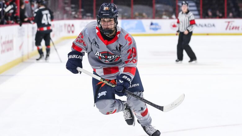 A female hockey player skates up the ice with both hands on her stick.