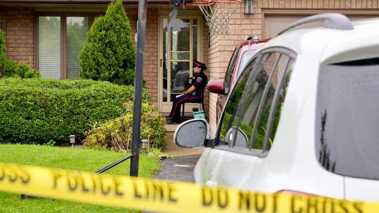 A Hamilton police officer sits outside the door to a home where, police say, a 16-year-old was stabbed during a family gathering.