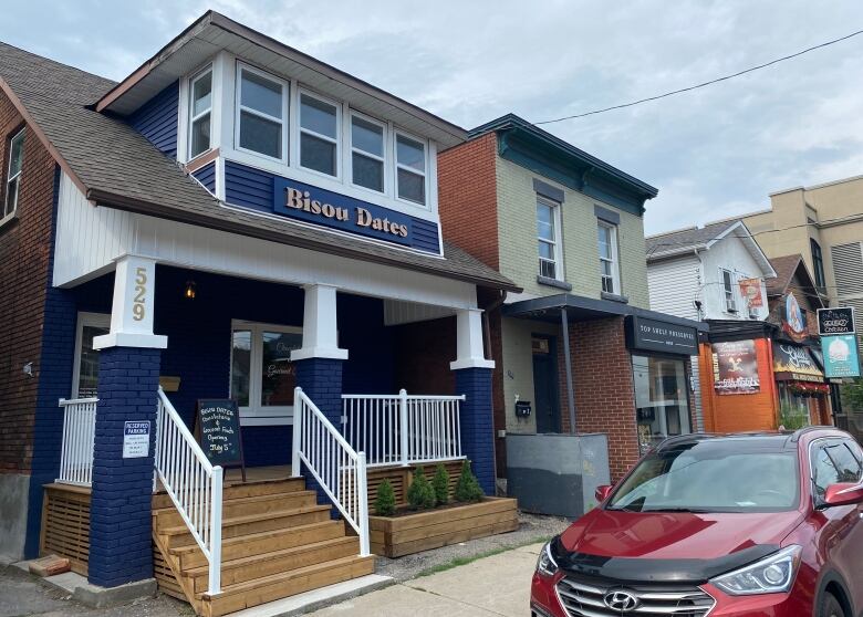 A blue and white-painted storefront of a business called Bisou Dates. Other businesses can be seen next door. A red car is parked in front.