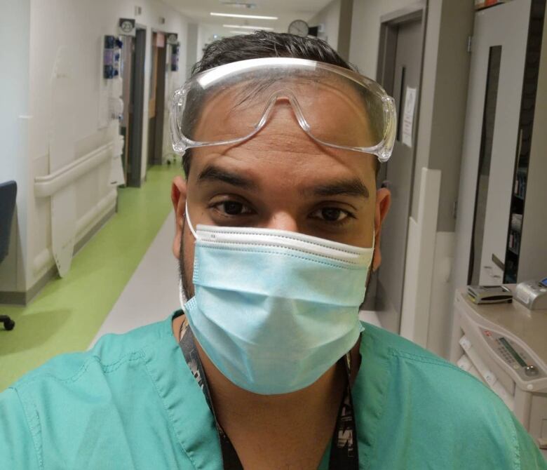 A selfie of a man in a hospital wearing green scrubs, a mask and a protective eye glasses. 