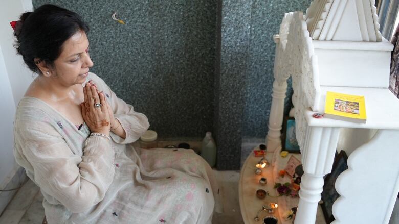 A person with closed eyes prays before a small shrine in their home.