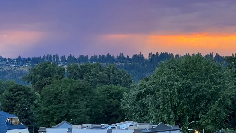 Wideshot of purple-coloured clouds with a ray of sunshine above buildings.