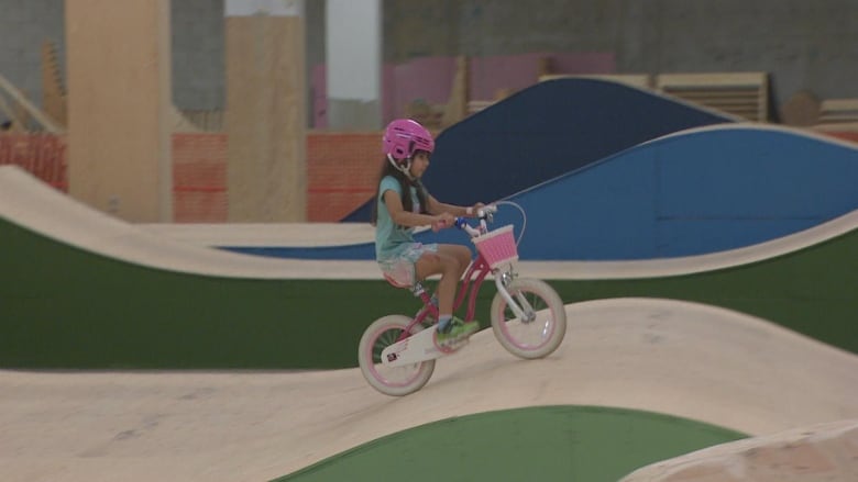 A young girl is pictured riding on a slope in the indoor bike park on a pink bicycle. 