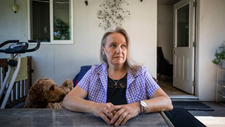 An older white woman sits on a patio deck with a brown dog next to her.