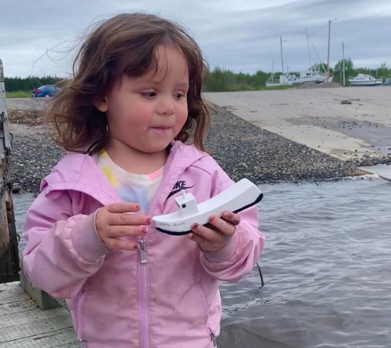 A girl in a pink sweater holds a little white boat. 