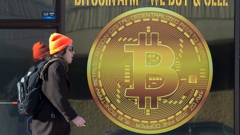 A person walks passed a Bitcoin logo.