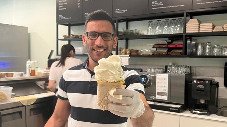 A man stands in an ice cream shop smiling, holding out an ice cream cone. 