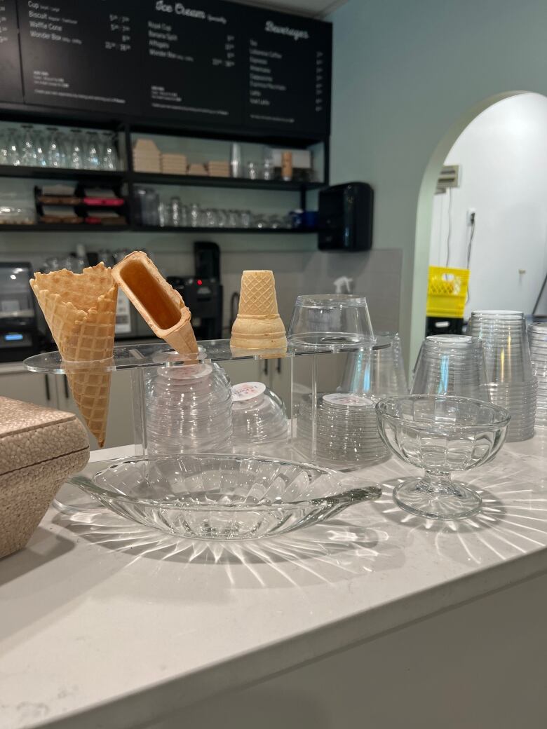 The counter of an ice cream shop closeup shows three ice cream cones on display: one waffle, one regular, and one slender and flat cone. 