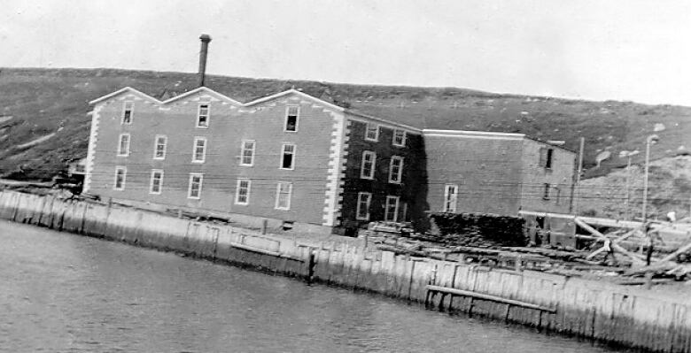 An old black and white image of a factory on the water.