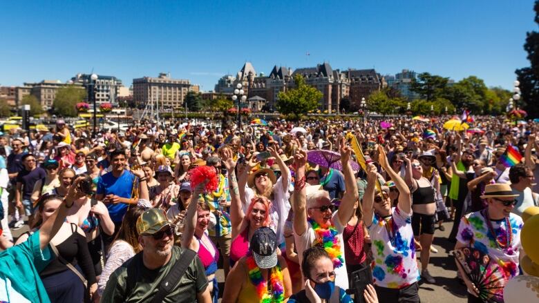 A large crowd of people cheer and raise arms in a large open area with buildings in the background.