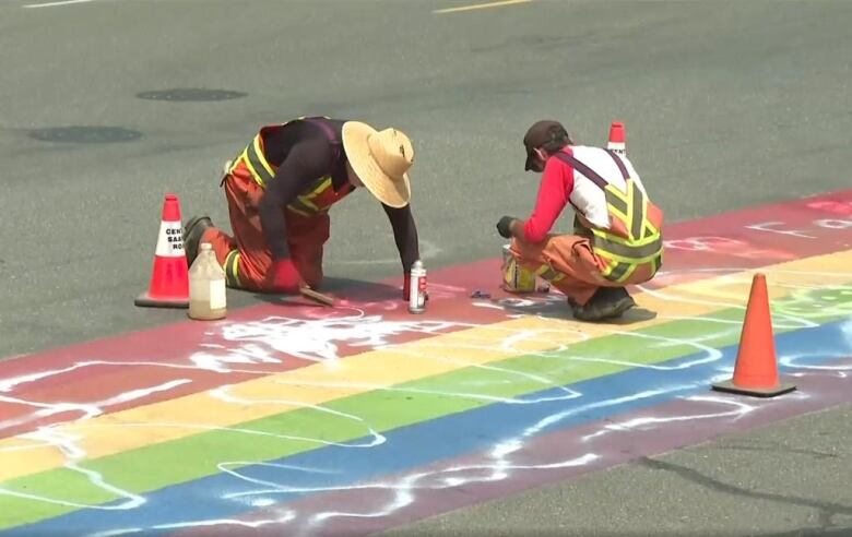 Two people are picture working on white paint graffiti on rainbow-coloured ground.