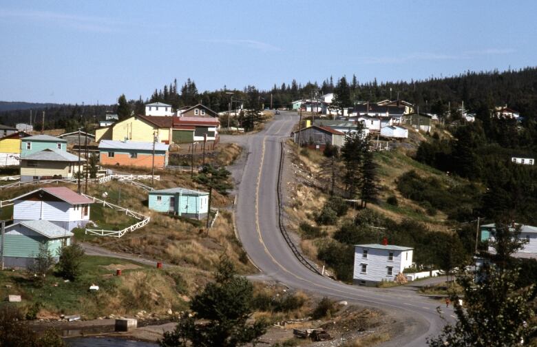 A two-lane paved road winds up a hill, past brightly painted houses on either side.