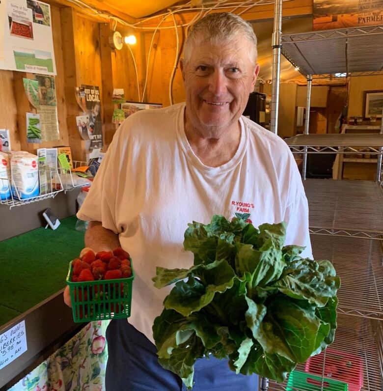 A 71-year-old man holds strawberries in one hand and lettuce in the other.