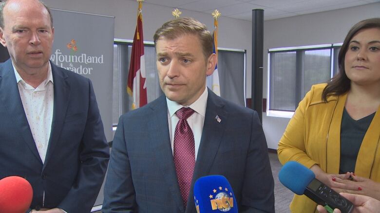 Three people stand in a conference room next to microphones.