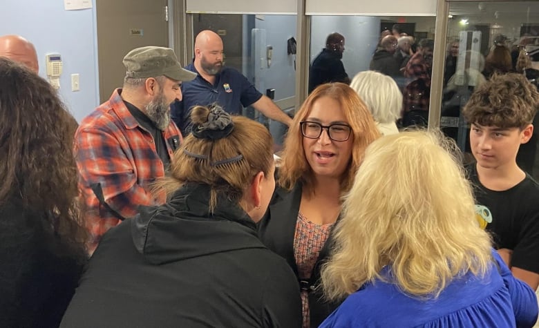 A woman speaks to several people surrounding her.