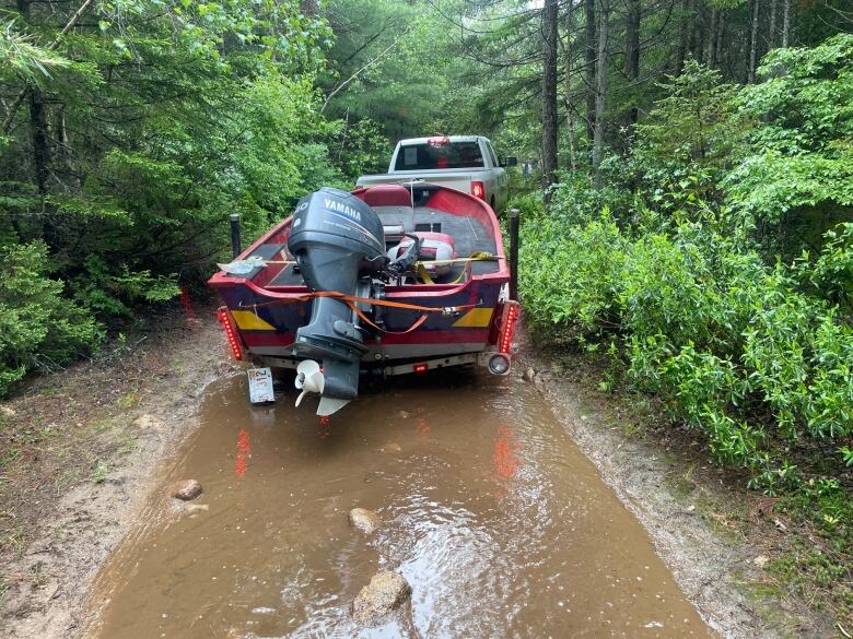 A truck pulling a small motorboat through the woods.