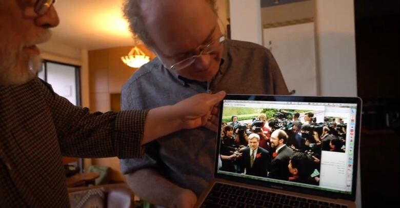 Two men hold a laptop with wedding photos on display.