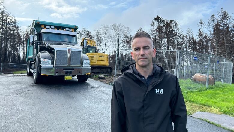 A man is shown in front of a fenced off property where his burned down house used to be in Westwood Hills, Nova Scotia with an excavator working.