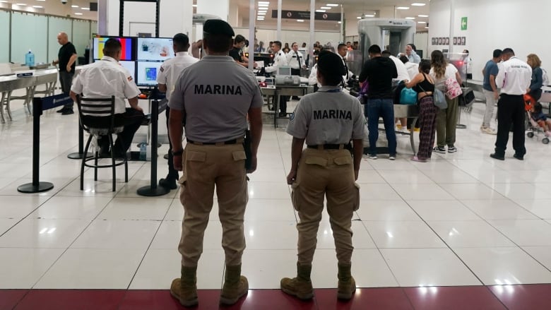 Two navy officers stand with their backs to the camera at an airport.