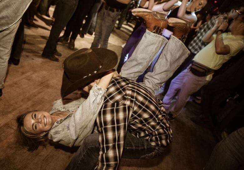 A women in a denim shirt being swung backward by a dance partner in a plaid shirt and jeans on a wooden dance floor.