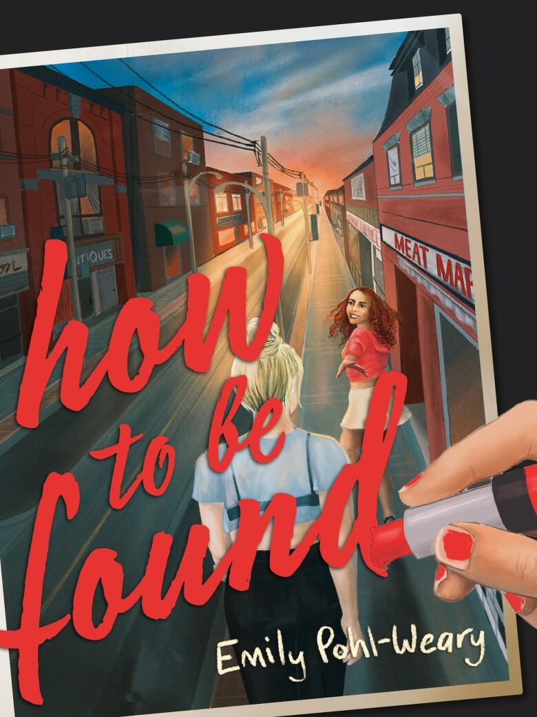 A book cover shows a photograph of two teenagers walking outside on the sidewalk of a town, with dusk lighting. A hand is writing the book's title over the photograph in red lipstick.