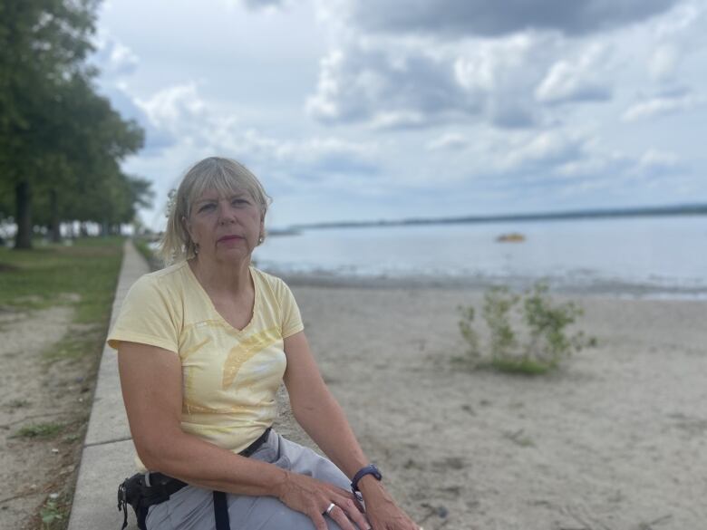 Woman in yellow shirt sits on concrete barrier.