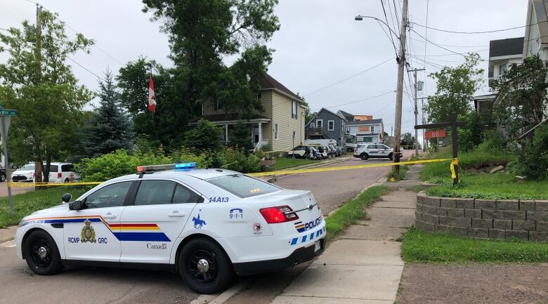 Police cars parked along a residential street with yellow crime scene tape across the road. 