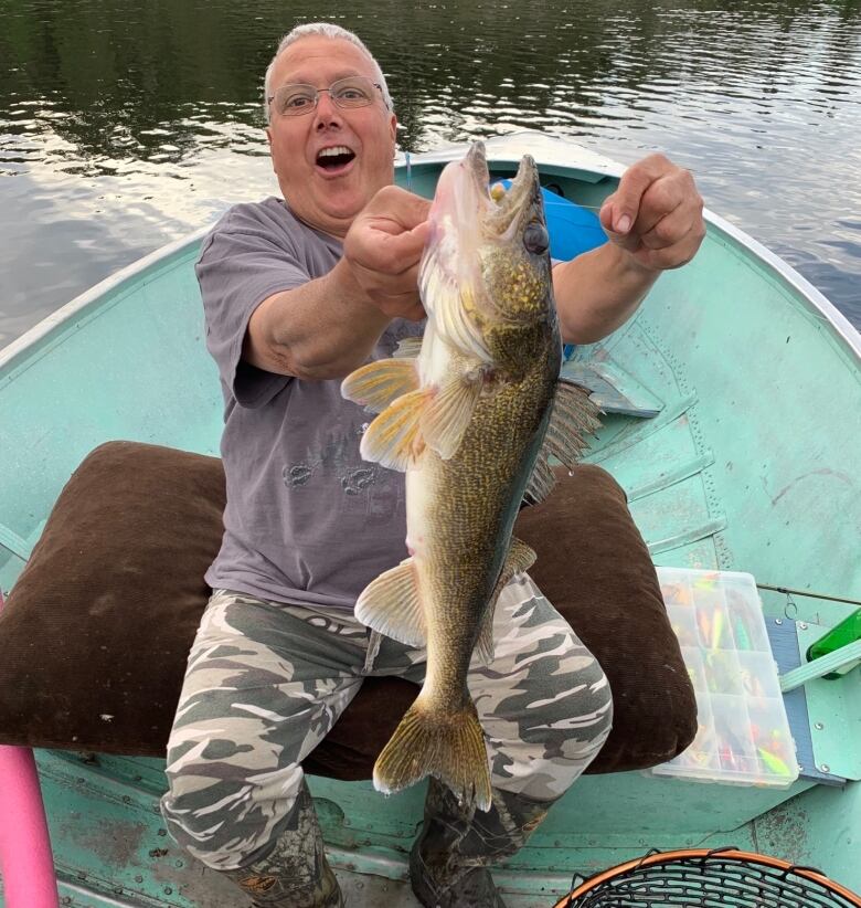 A man holds a fish, with an excited expression on his face. 