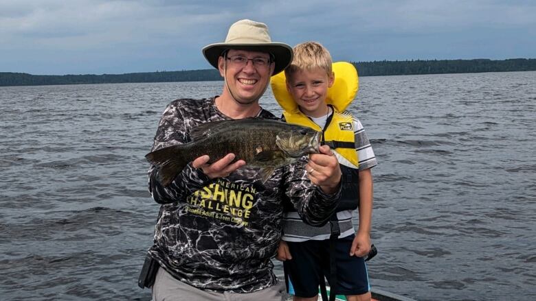 A father and son hold a fish. 