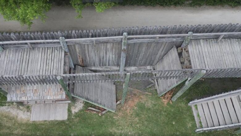 Sections of a raised wooden walkway are seen broken away and lying on the ground. 