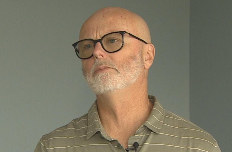 bald man with glasses in front of grey wall