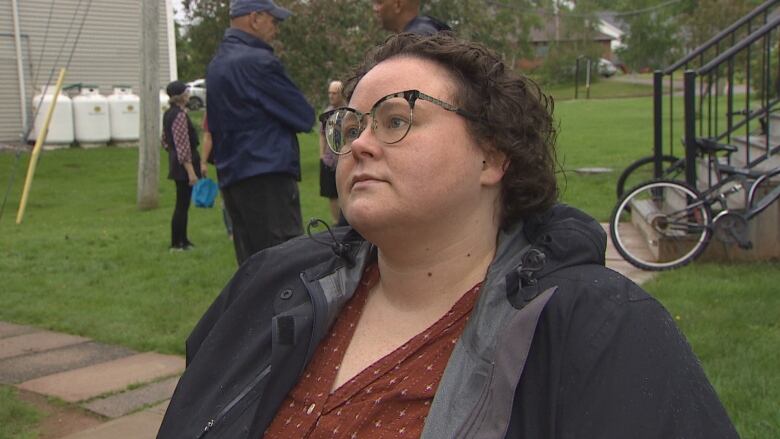 Kim Mears looks at reporter off camera. She's wearing a red shirt and grey raincoat.