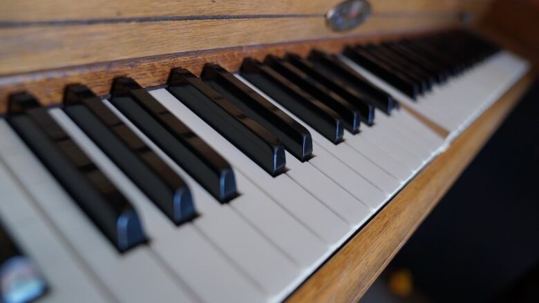 A closeup shows the white keys of a piano, with one key depressed.