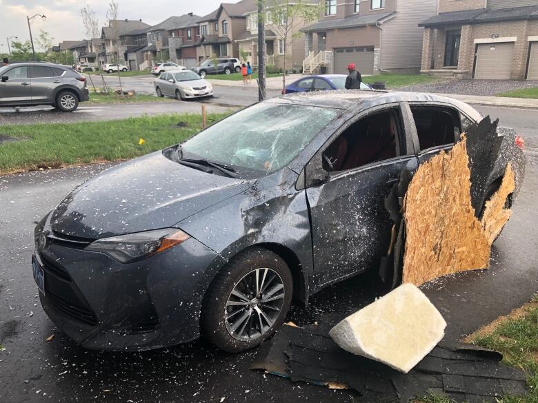 A dented car on a driveway with a piece of broken wood next to it.