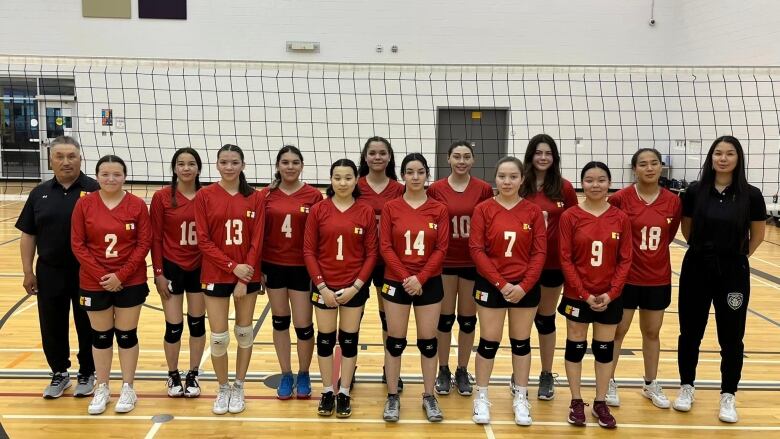 A team of young women who are part of Team Nunavut's volleyball team from pose in front of a volleyball net.