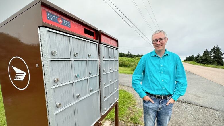 A man with a blue long-sleeved shirt and glasses stands next to a Canada Post community mailbox.