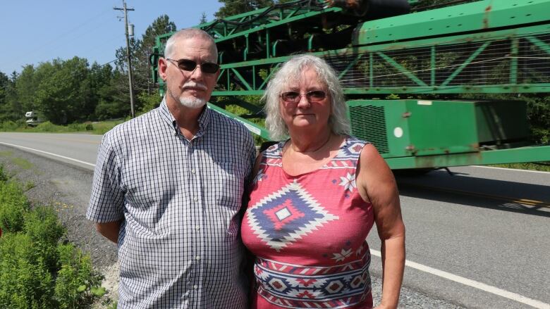 Two people stand by the side of the road with a truck zooming by in the background.