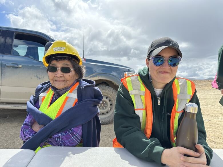 Two women in safety gear sit at a table outside.