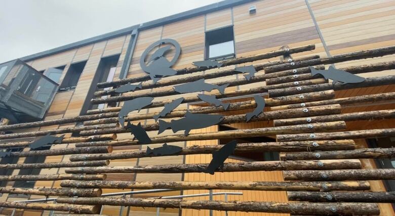 Wooden poles made into a fence that represent fish drying racks with black salmon covering it.