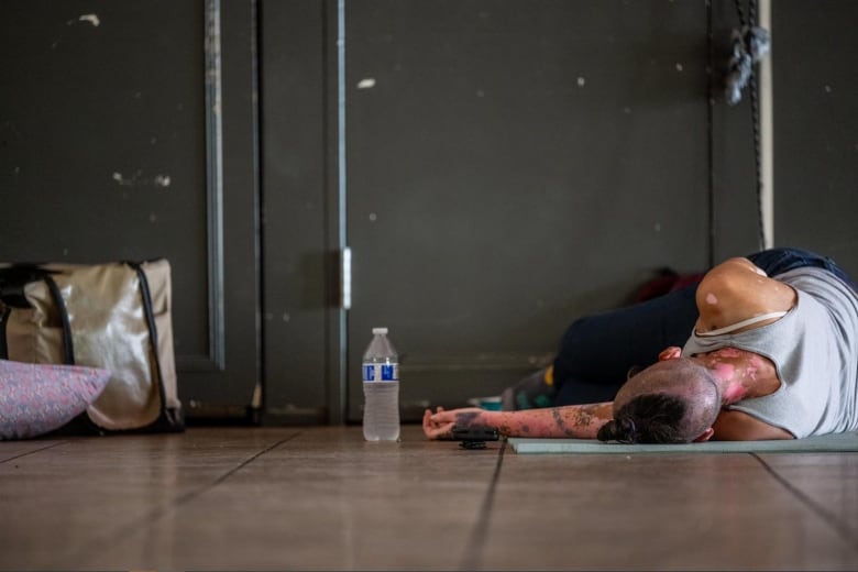 A person lies on the ground next to a bottle of water.