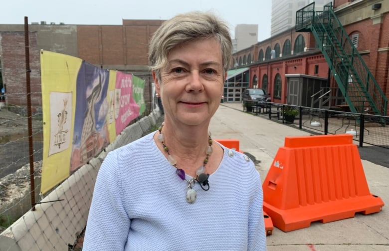 Head and shoulders picture of a woman standing in front of a fenced off construction area without construction. 