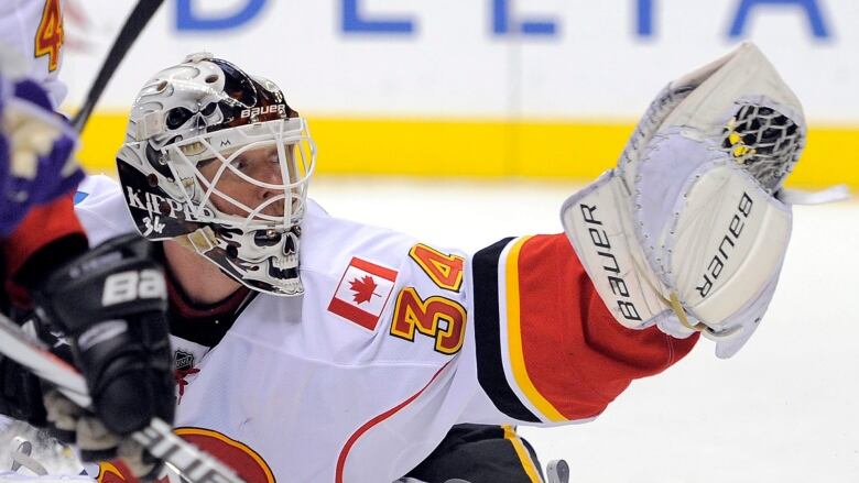 A hockey goalie reaches with his glove hand to save a puck from going in the net. He is staring at the glove as the puck enters it.