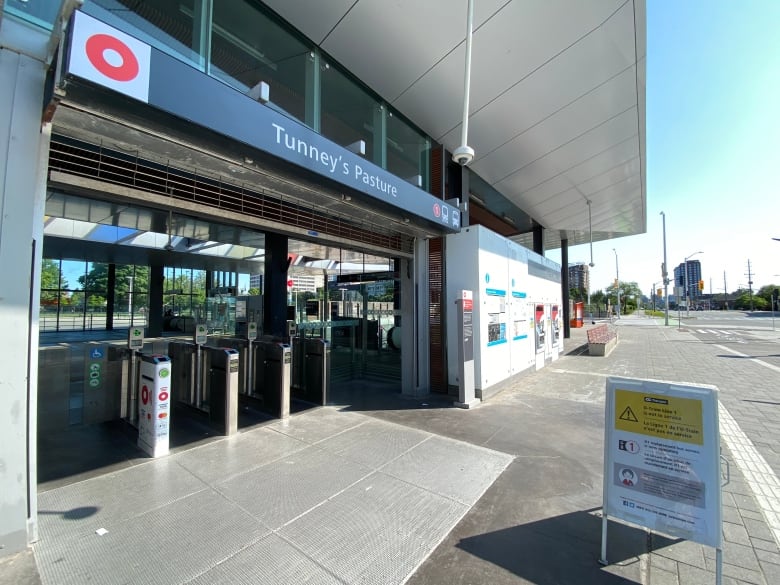 A white and yellow sign outside a closed light rail station on a summer day.