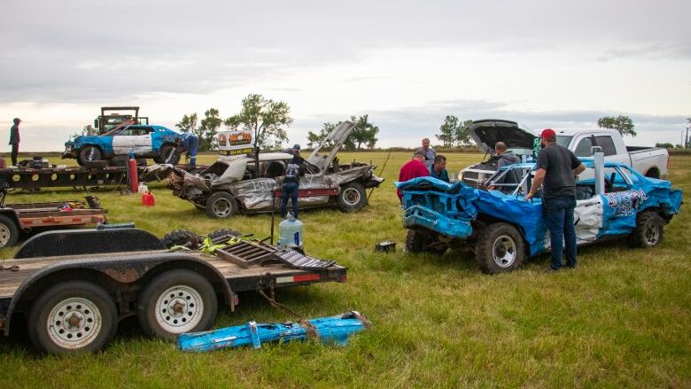 A group of people work on three derby cars.