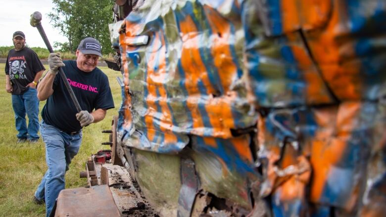 A man takes a sledge hammer to a derby car.